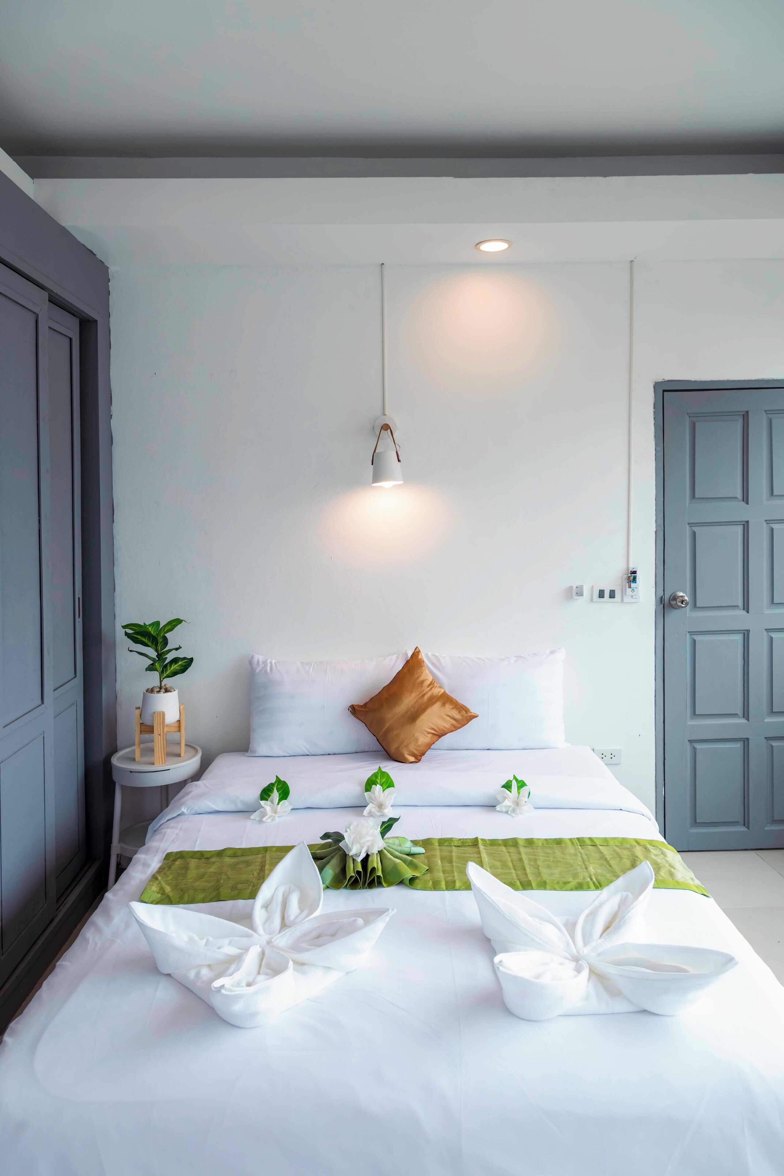 Una cama bien tendida con sábanas blancas, un plaid verde y flores blancas decorativas.
