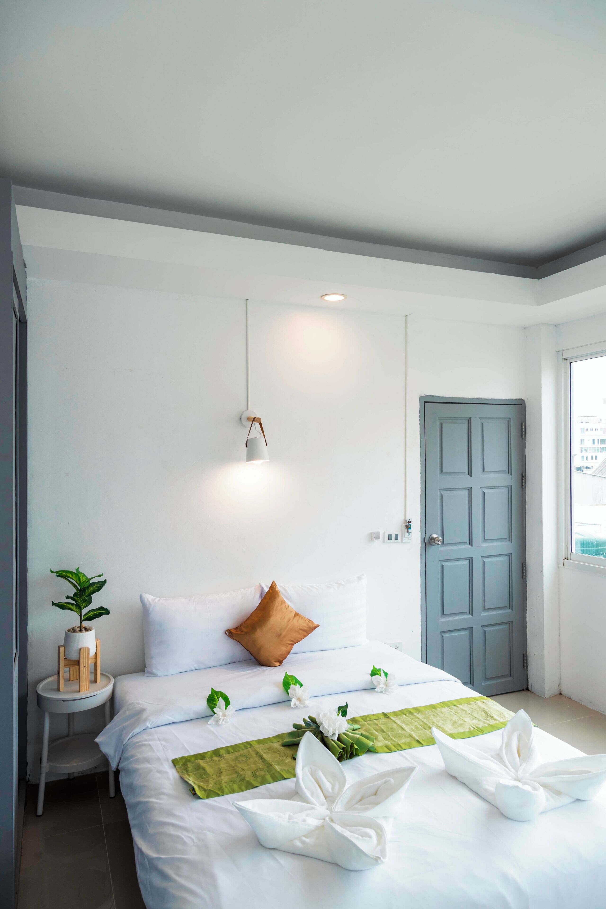 Une chambre d’hôtel bien rangée, avec un lit, une table de chevet, une plante en pot et une porte.