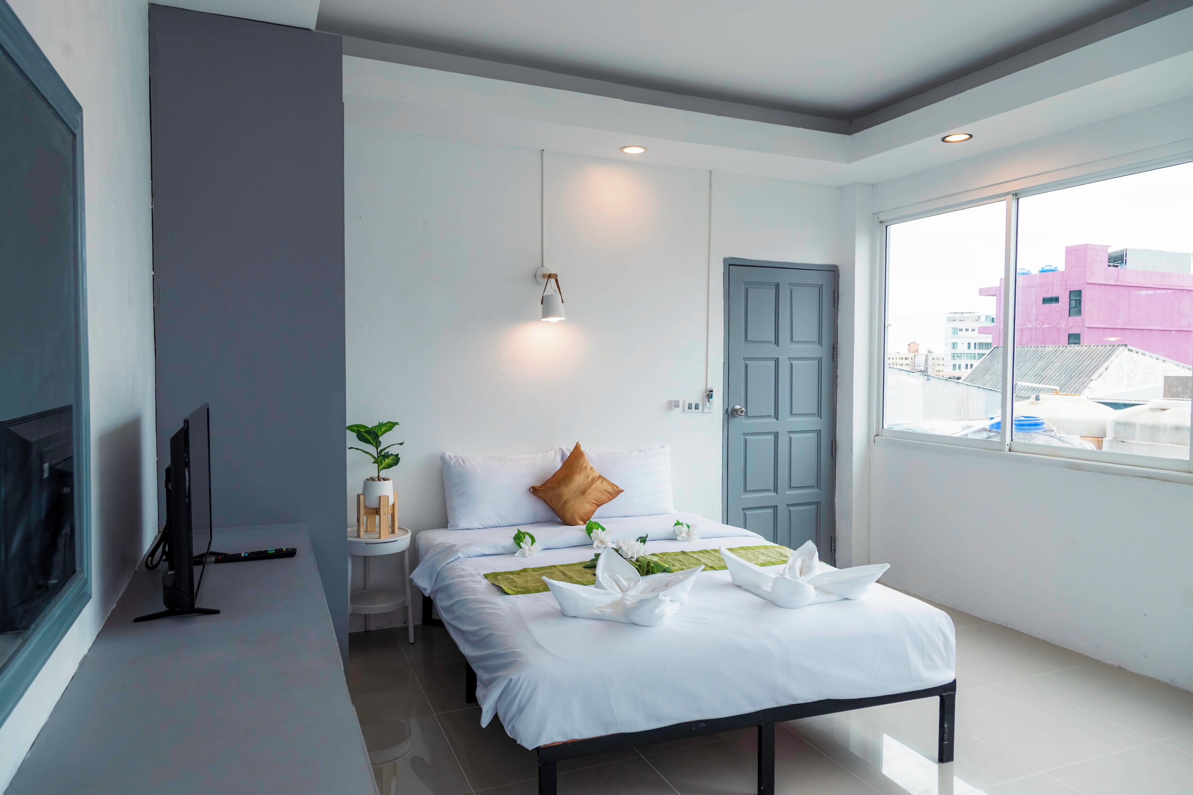 Een moderne hotelkamer met een bed, een televisie, een raam met uitzicht op de stad en een deur.