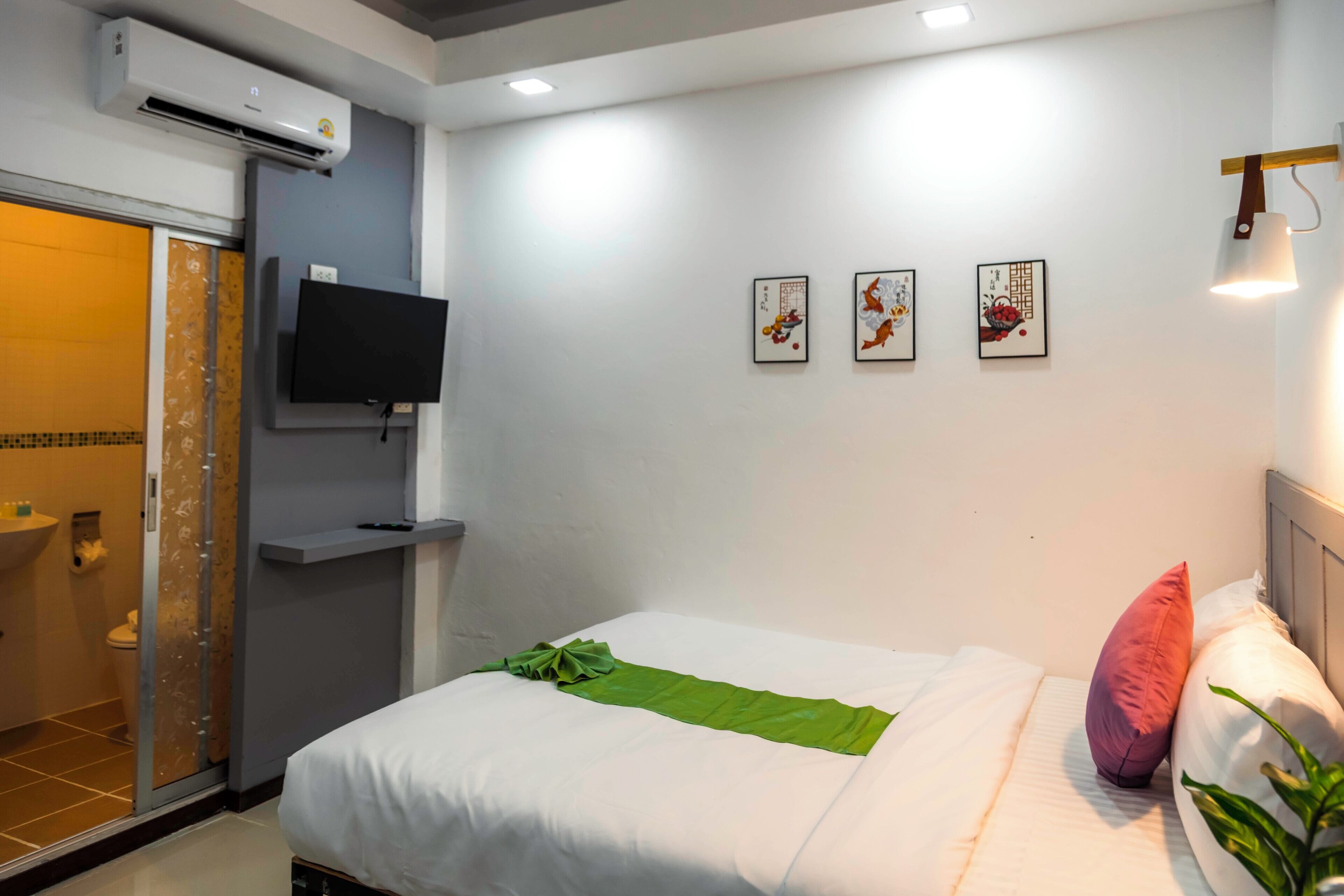 A hotel room with a bed, a flat-screen TV, a shower, and three framed artworks on the wall.