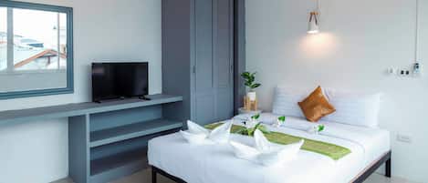 Una habitación de hotel moderna con una cama, un televisor en un mueble bajo, un armario gris, una mesita con una planta y vistas a edificios.