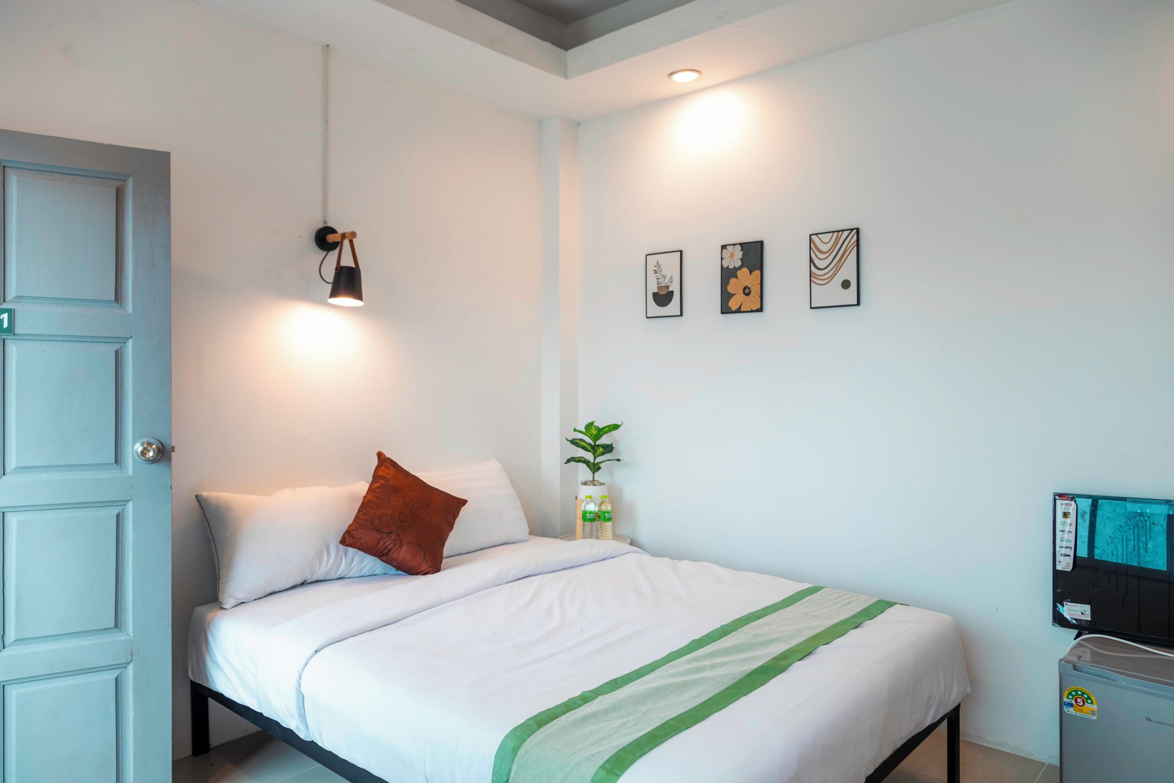 A hotel room with a bed, a wall-mounted TV, and a door with a number.
