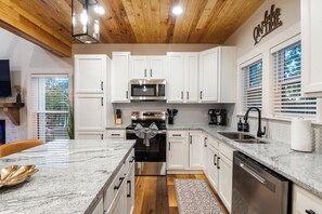 A modern kitchen with white cabinets, stainless steel appliances, a granite countertop, and a wooden ceiling.