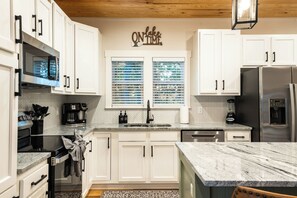 A modern kitchen with white cabinets, a granite countertop, a built-in oven, a coffee maker, and a refrigerator. - Nolin Lake Views | Hot Tub + EV Charger + Games (Clarkson)