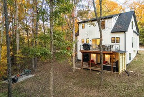 A two-story house with a deck, surrounded by trees with autumn foliage.