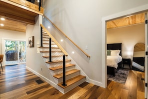 Ein modernes Interieur mit einer Holztreppe, einem Bett mit Nachttisch und Blick ins Freie.