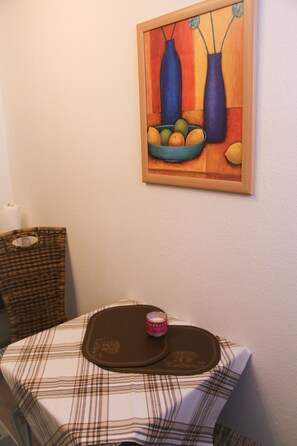 A dining table with a plaid tablecloth, a placemat, and a candle. A painting of vases and fruits hangs on the wall. - Apartment 'Talblick' with Wi-Fi (Meßstetten)