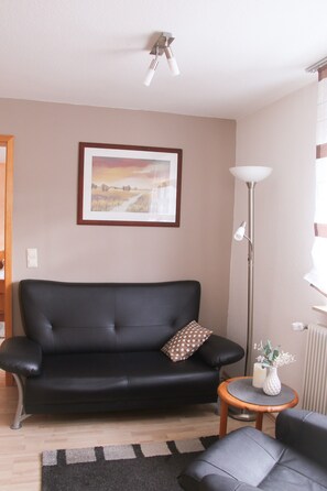 Ein Wohnzimmer mit einer schwarzen Ledersofa, einem kleinen runden Holztisch mit einer Vase und einer Stehlampe.
