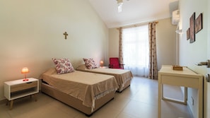 A hotel room with two beds, a desk, a chair, and a cross on the wall. - Villa Lagoon by Oazure (Trou d'eau douce)