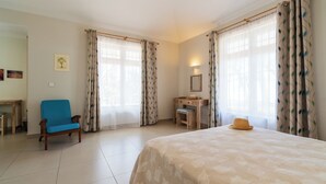 Una habitación de hotel con cama, escritorio, silla y ventanas amplias con cortinas.