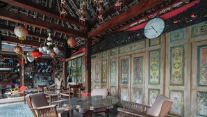 Un intérieur traditionnel avec une table ronde en verre entourée de chaises en bois, un plafond en bois avec des poutres apparentes et des décorations murales élaborées.