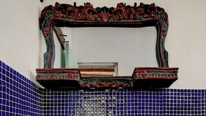 Une salle de bain dotée d’un grand lavabo rustique, de carreaux de mosaïque bleus et d’un miroir décoratif placé au-dessus du lavabo.