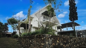 Une maison moderne avec un mur de pierre au premier plan, un balcon et un ciel bleu dégagé.