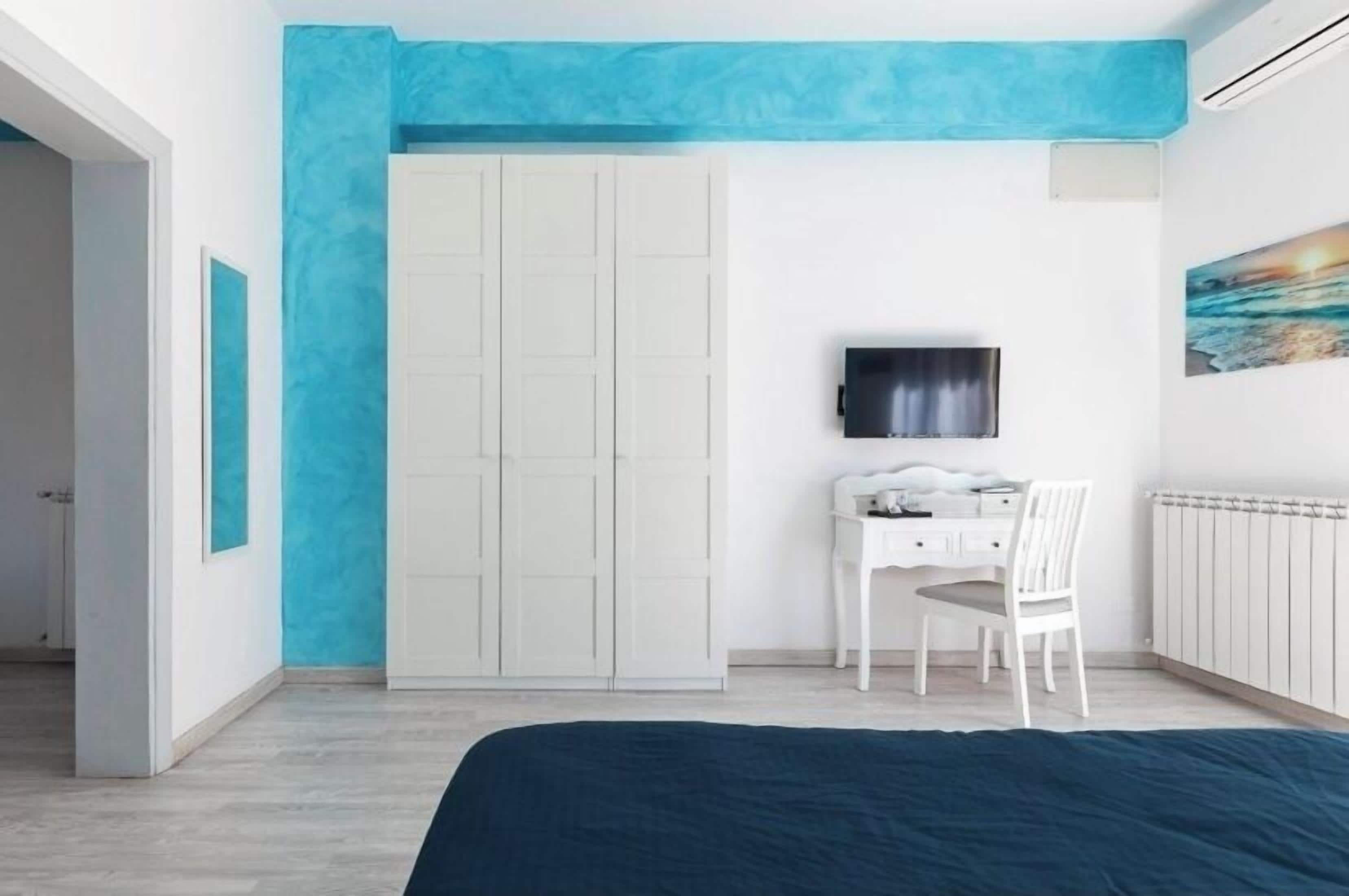 Ein Schlafzimmer mit Bett, Schreibtisch, Stuhl, Kleiderschrank, Fernseher und einem Bild an der Wand.