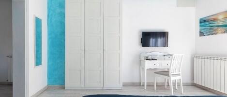 Un dormitorio con cama, escritorio, silla, armario, televisor y un cuadro en la pared.