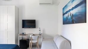 Hotellihuone, jossa on sänky, työpöytä tuolilla, televisio ja taulu seinällä.