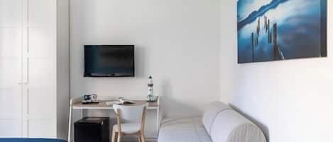 Habitación de hotel con cama, escritorio con silla, televisor y un cuadro en la pared.