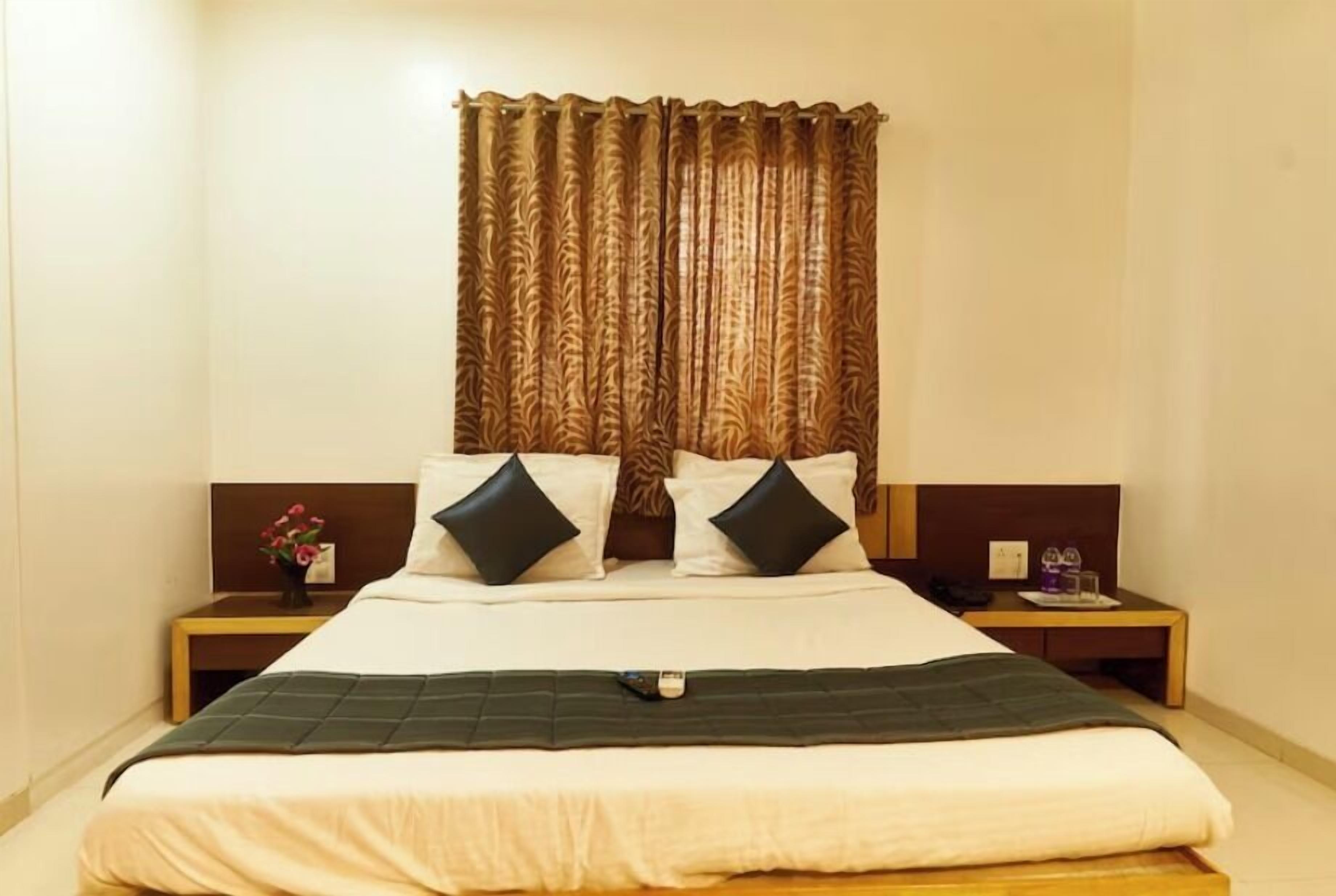 A neatly made bed with a dark headboard, two pillows, and a bedside table with a lamp and a small vase of flowers.
