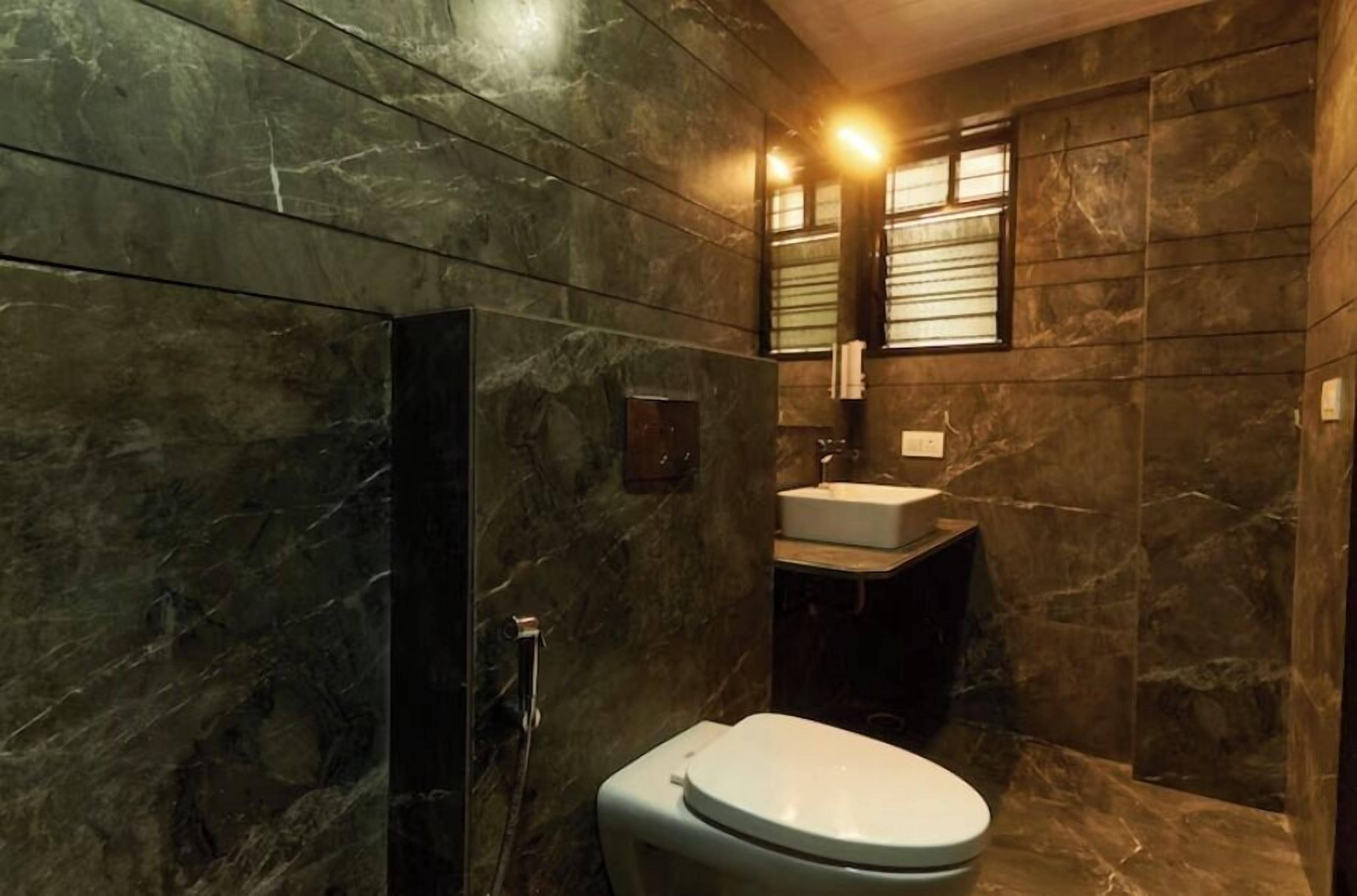 A bathroom with a marble wall, a toilet, a sink, and a shower area.