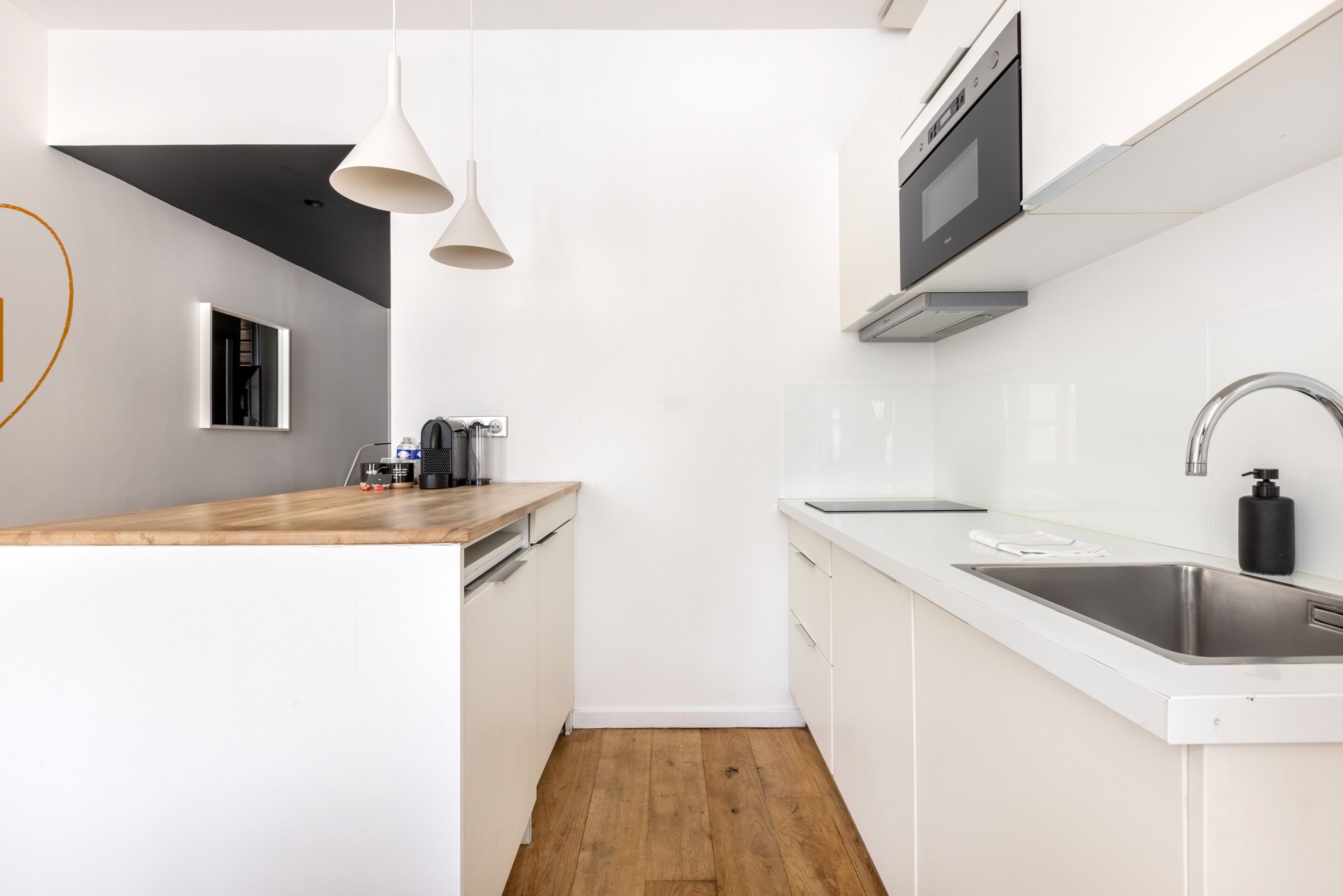 Una cocina moderna con armarios blancos, encimera de madera, pileta de acero inoxidable e iluminación colgante.