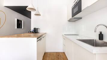 Una cocina moderna con armarios blancos, encimera de madera, pileta de acero inoxidable e iluminación colgante.