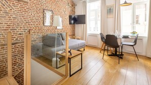 Un salon moderne avec un mur en briques, un canapé, une table basse en verre, un téléviseur et un coin repas avec des chaises et une table.