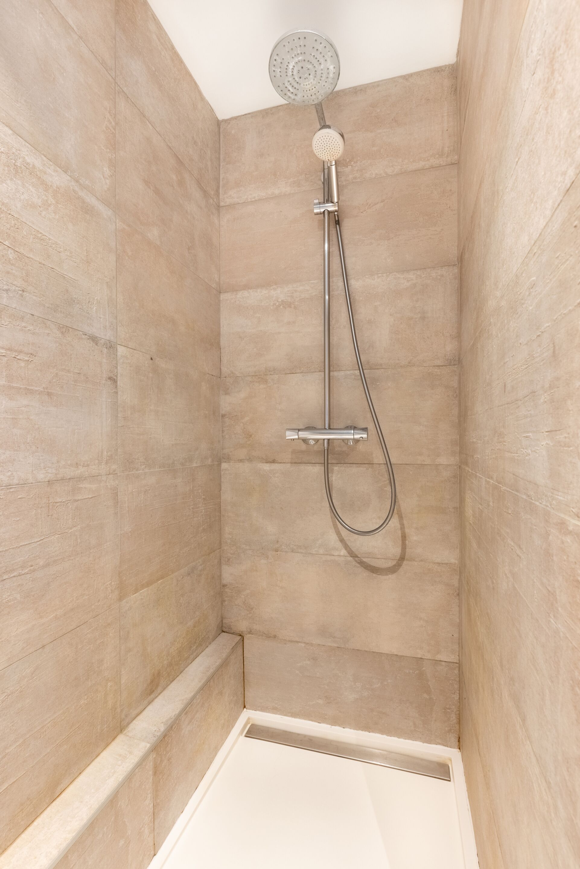 A shower with a handheld showerhead and a wall-mounted faucet in a tiled room.