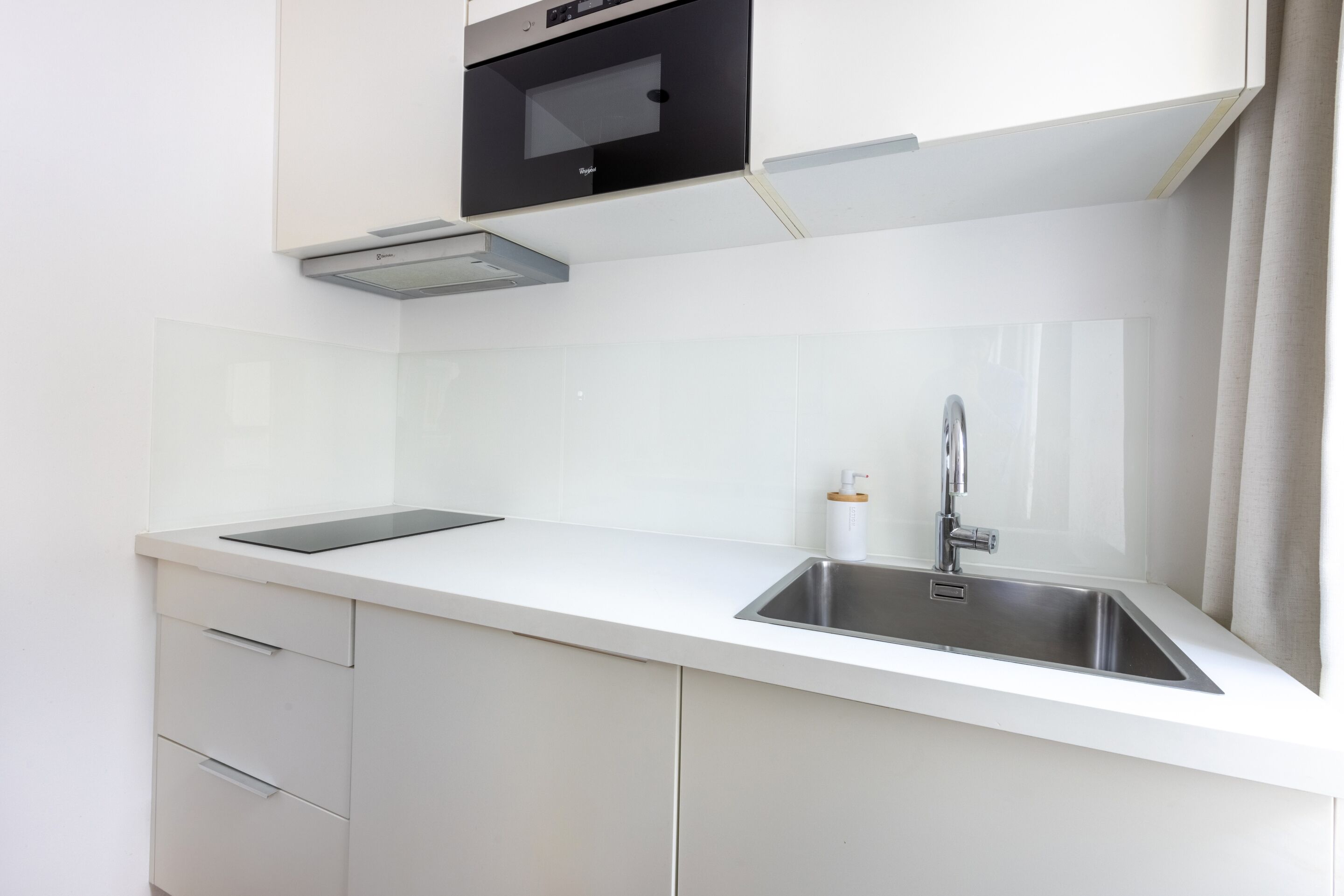 A modern kitchen with white cabinetry, a stainless steel sink, and a built-in oven.