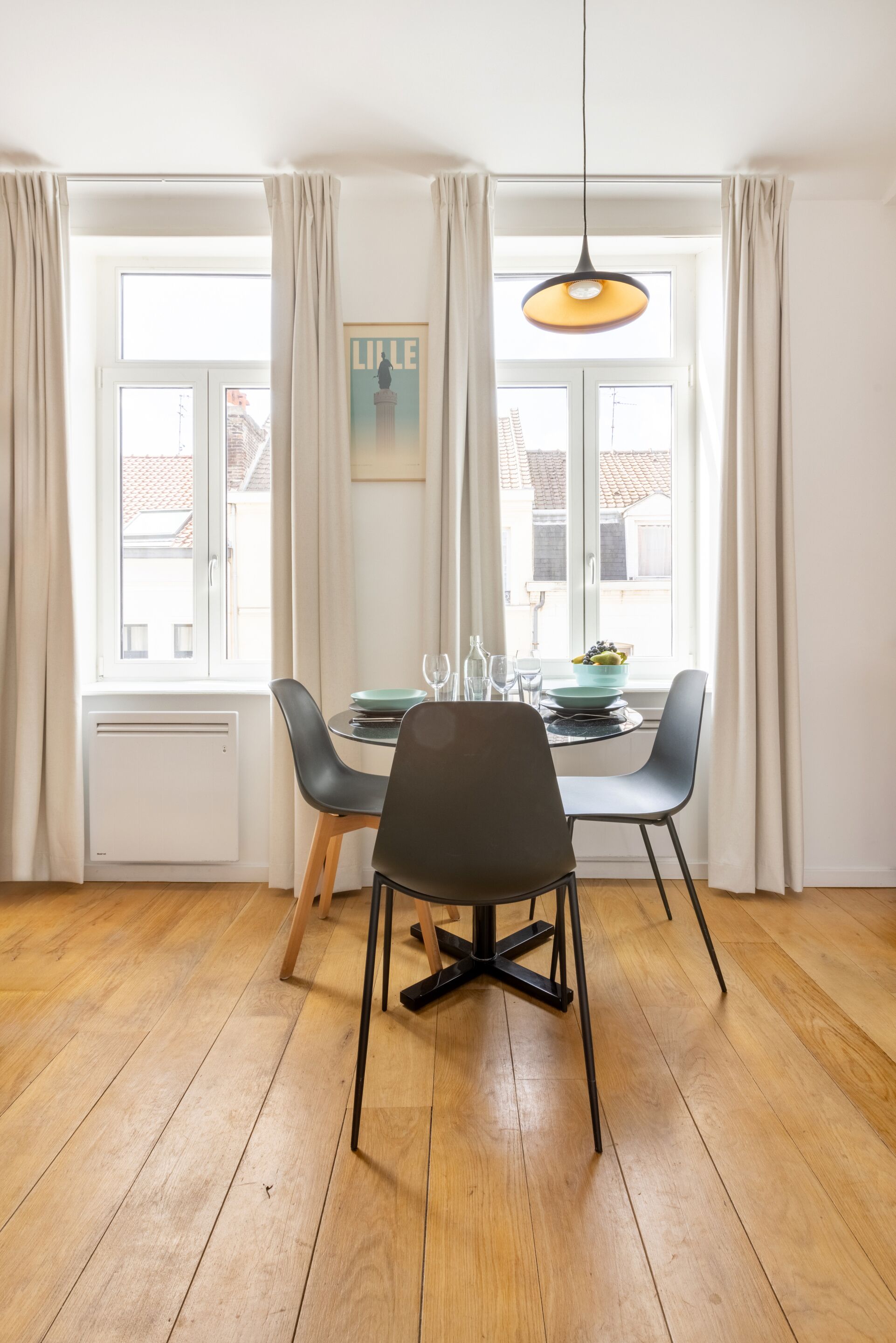 Comedor con mesa, sillas, lámpara colgante y ventana con cortinas.