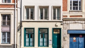 Une rangée d’immeubles à étages, chacun présentant un style architectural distinct, dont un bâtiment avec une porte verte portant l’inscription « Au Chat Quidort ».