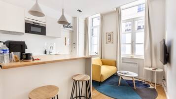 Una cocina moderna con microondas, horno y cafetera. En la zona de estar, hay un sofá amarillo y una pequeña mesa redonda.