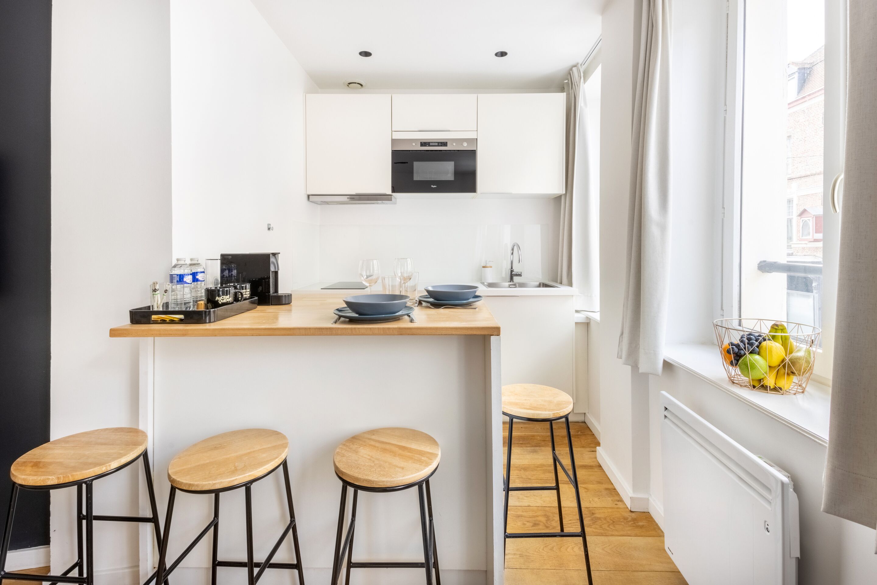 Una cocina moderna con armarios blancos, encimera de madera y tres taburetes.