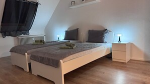 Un dormitorio con cama, mesitas de noche, un radiador y una ventana con cortina.
