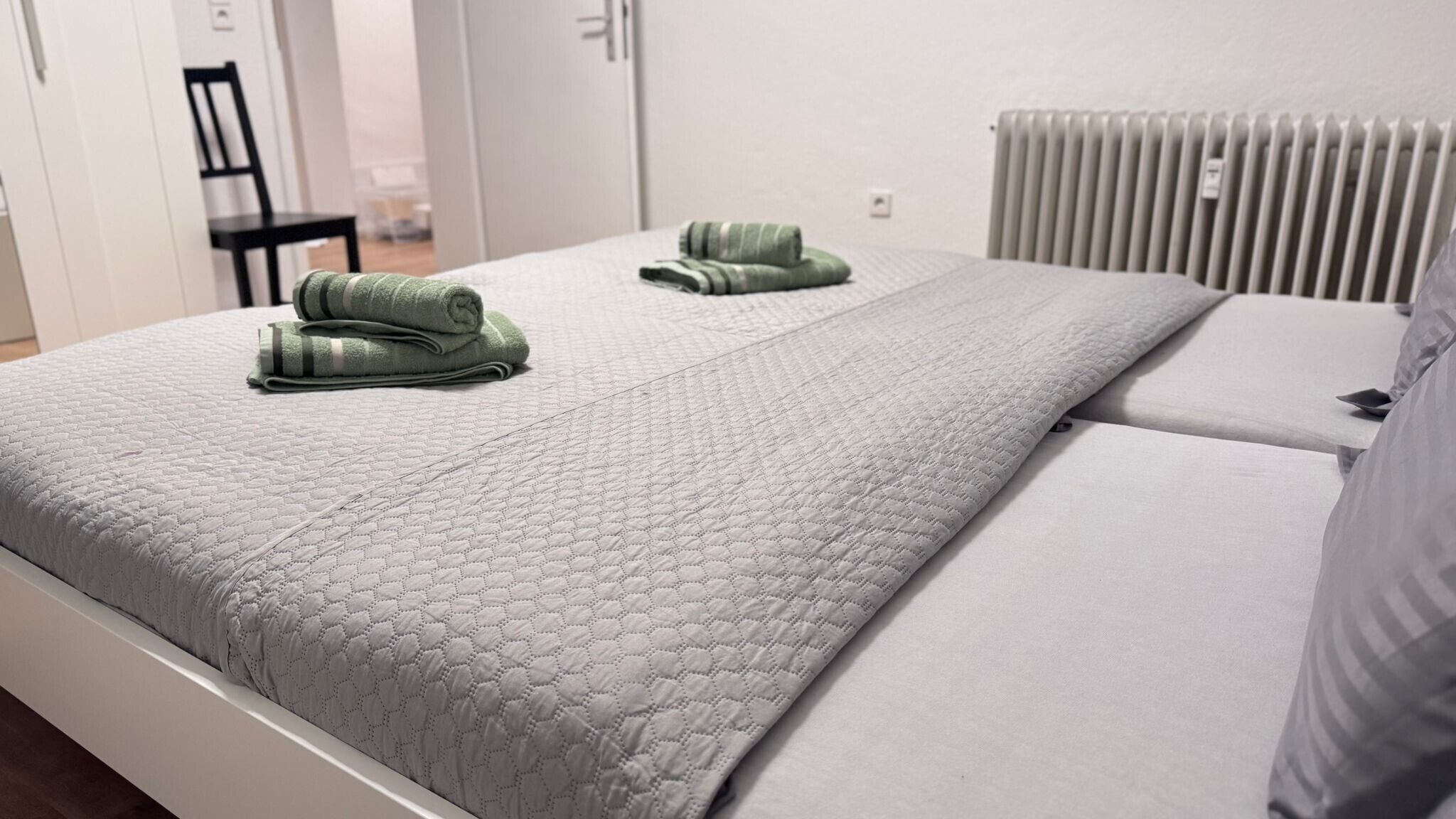 A bed with a quilted cover, a pillow, and two rolled-up towels.