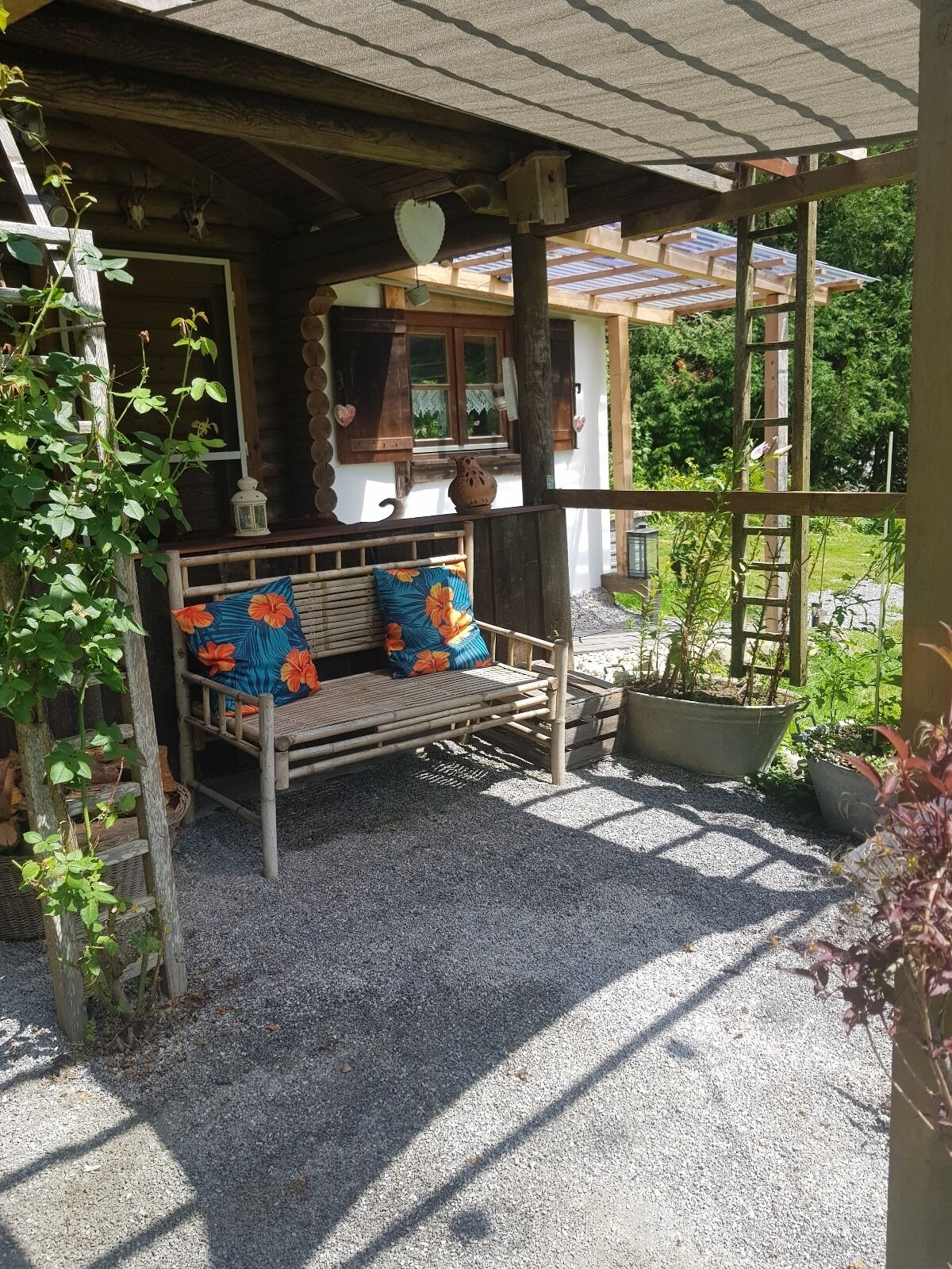A wooden bench with floral cushions, a rustic wooden structure with a sloped roof, and a garden area with potted plants.