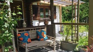 A wooden bench with floral cushions, a rustic wooden structure with a sloped roof, and a garden area with potted plants.