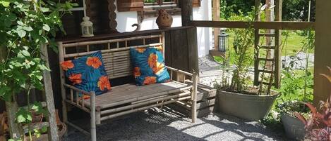 A wooden bench with floral cushions, a rustic wooden structure with a sloped roof, and a garden area with potted plants.