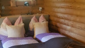 A cozy cabin-style room with a wooden interior, a bed with patterned bedding, and a window with a lace curtain.