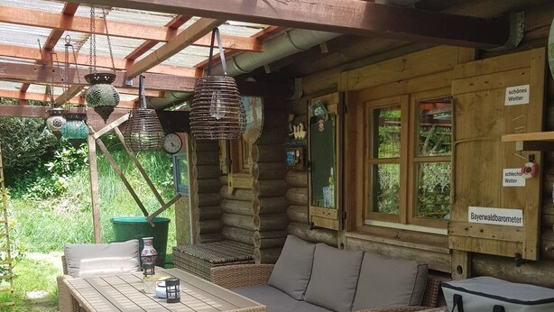 A log cabin with a wooden deck, wicker furniture, and a Bayerwaldbarometer sign.