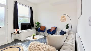 A modern living room with a sofa, two armchairs, a coffee table, and a large window with curtains.