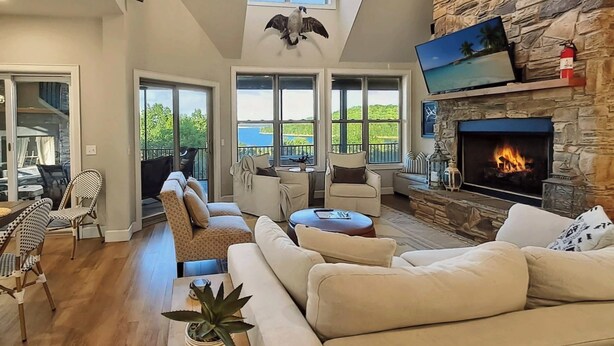 Un salón amplio con chimenea de piedra, asientos cómodos y ventanas grandes que ofrecen vistas al exterior.
