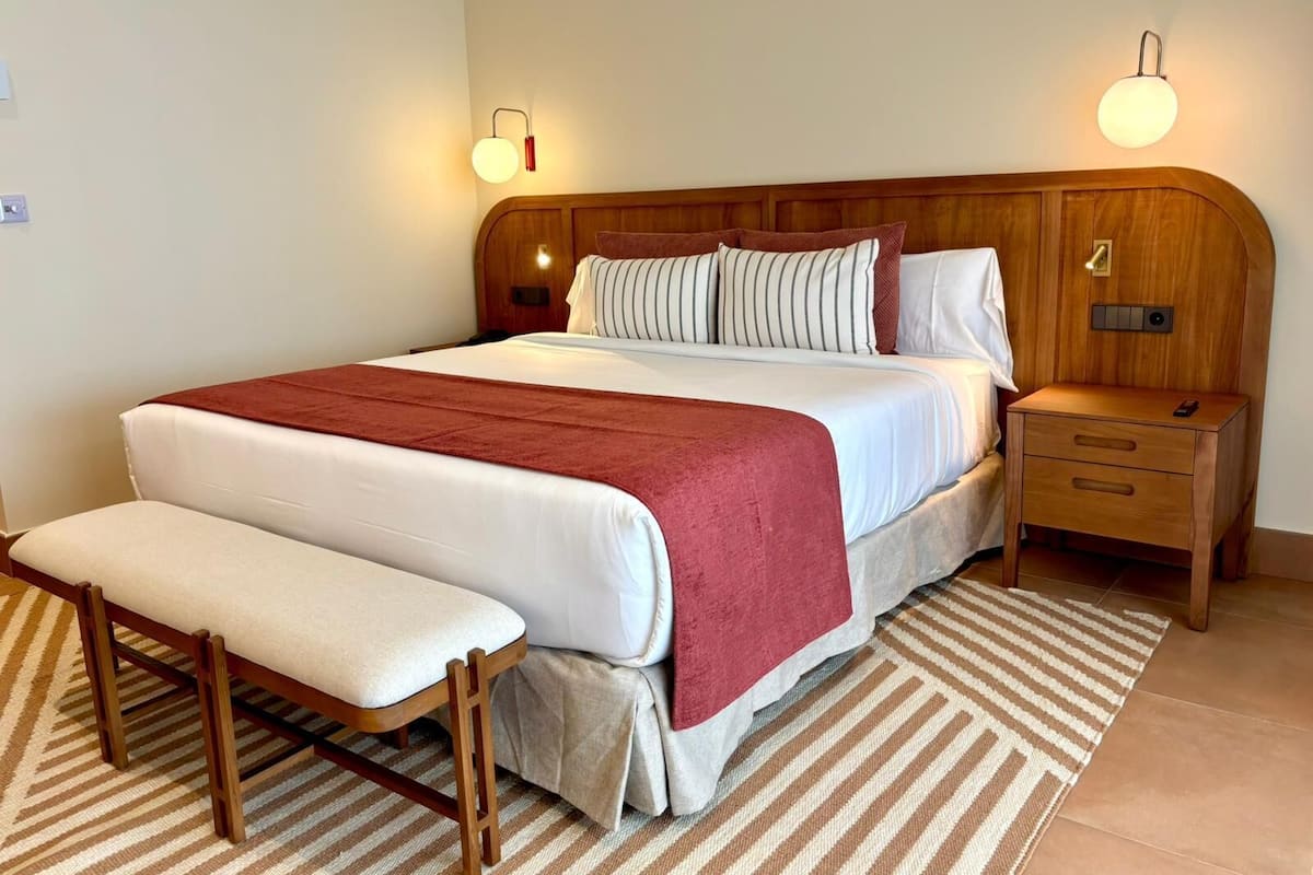 A neatly arranged bedroom with a wooden bed, a bench, two bedside tables, and a striped rug.