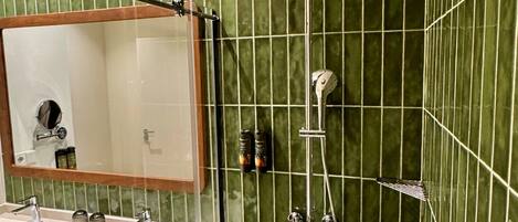 A bathroom with a green tiled wall, a shower, a sink with a mirror, and a towel rack.