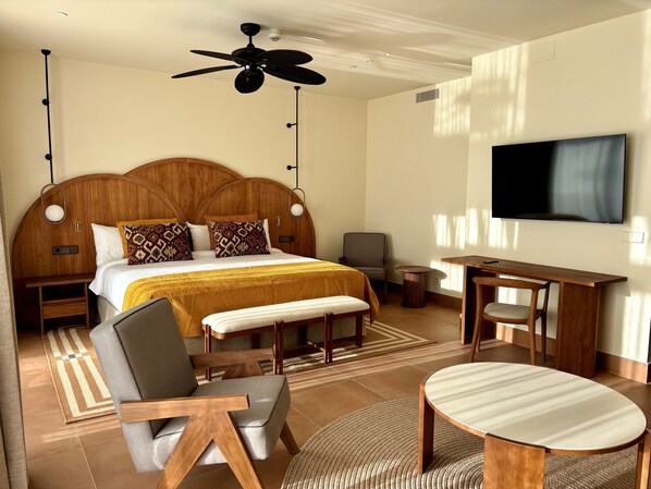 Une chambre d’hôtel avec un grand lit, un bureau, une chaise, une télévision et un ventilateur de plafond.