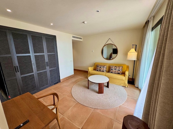 A living room with a sofa, a coffee table, a round rug, and a dining table. - Punta Bermeja Premium Beach Hotel (El Puerto de Santa Maria)