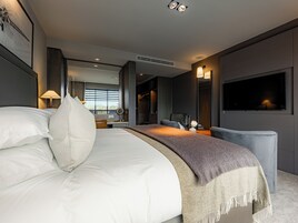 Una habitación de hotel moderna con una cama grande, un escritorio, una silla, un televisor y una ventana con persianas.