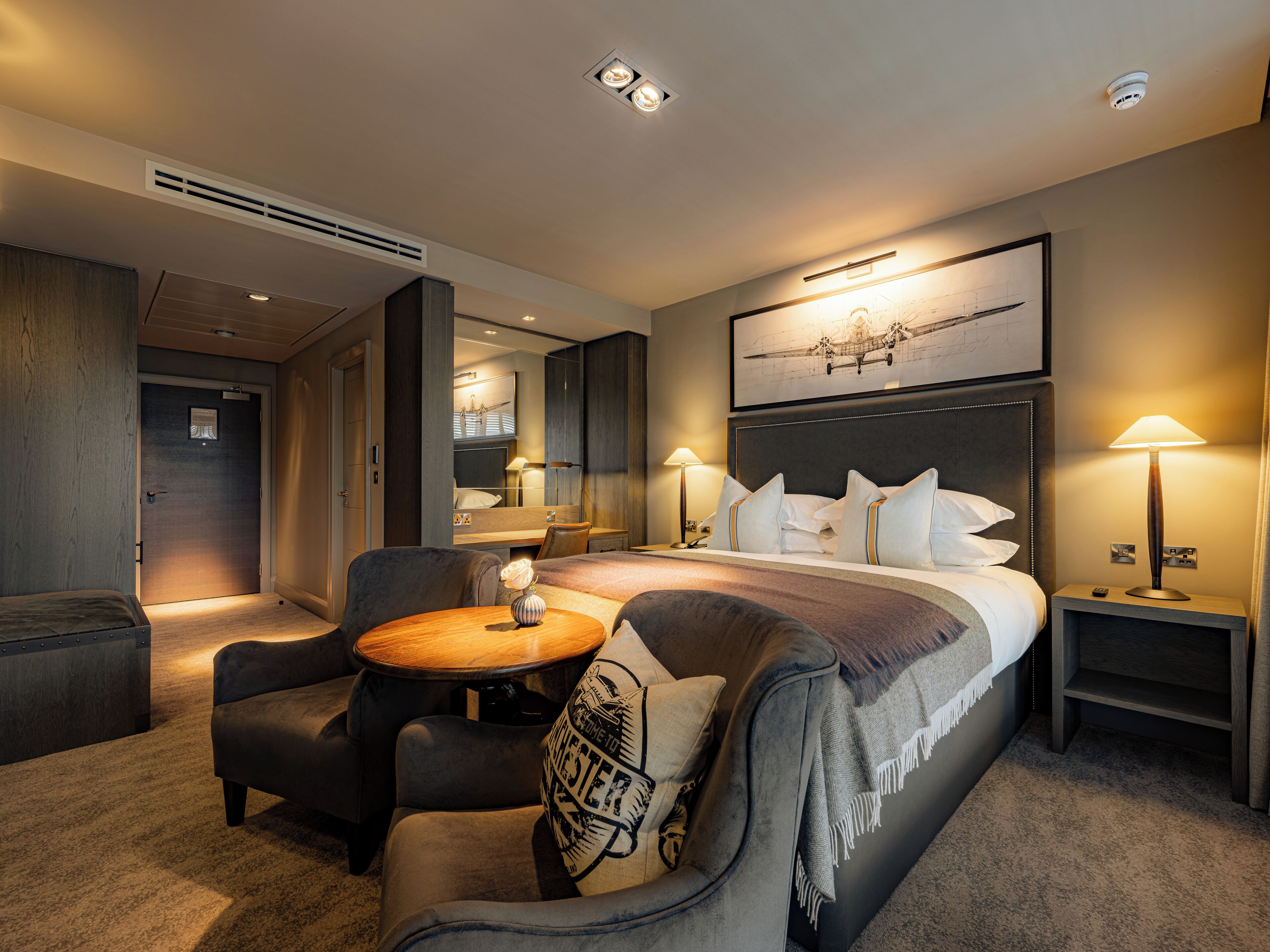 A hotel room with a bed, two bedside tables, a desk, a chair, and a small round table.