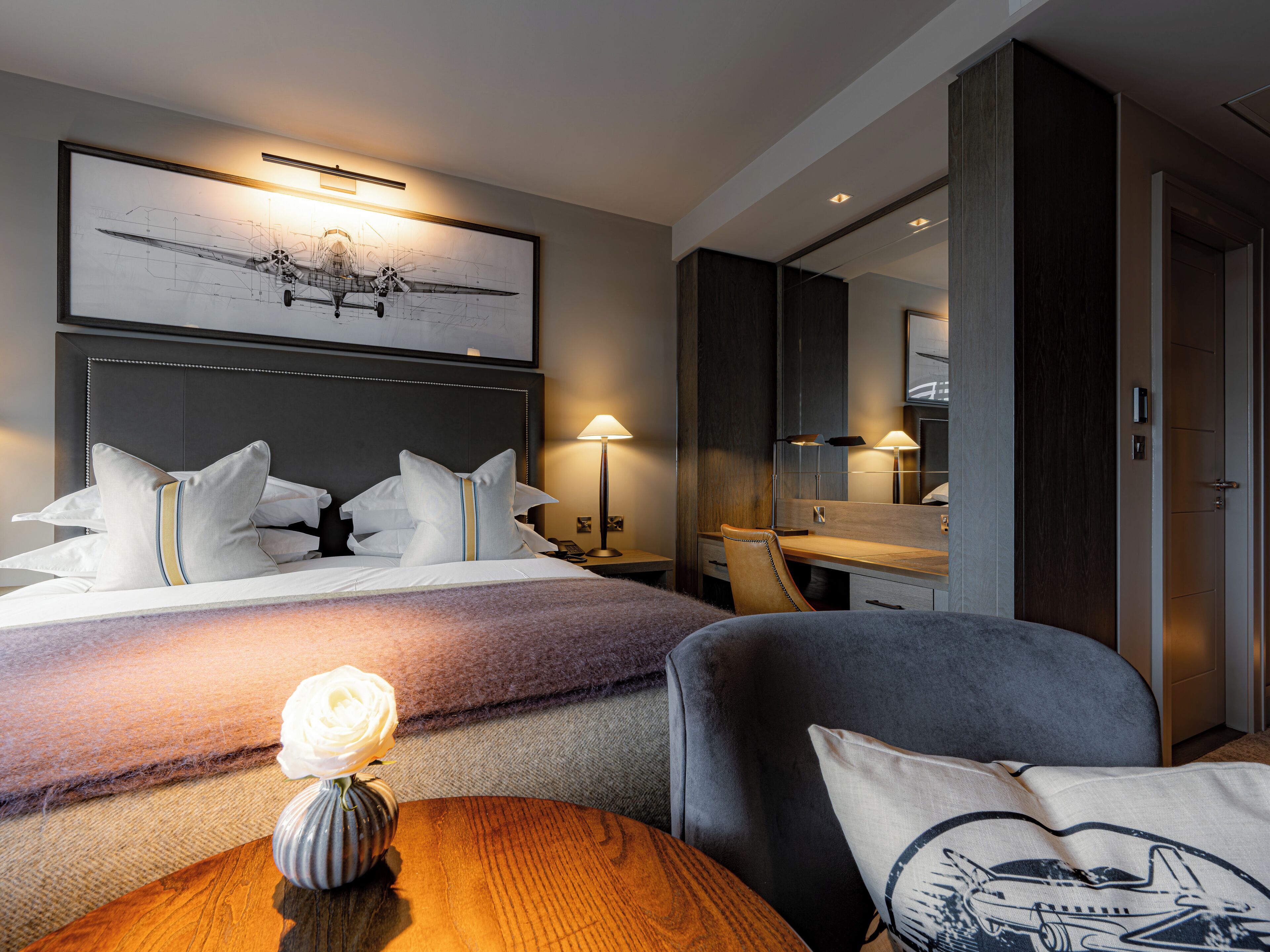 Quarto de hotel com cama, mesa de cabeceira, abajur e um espelho grande.