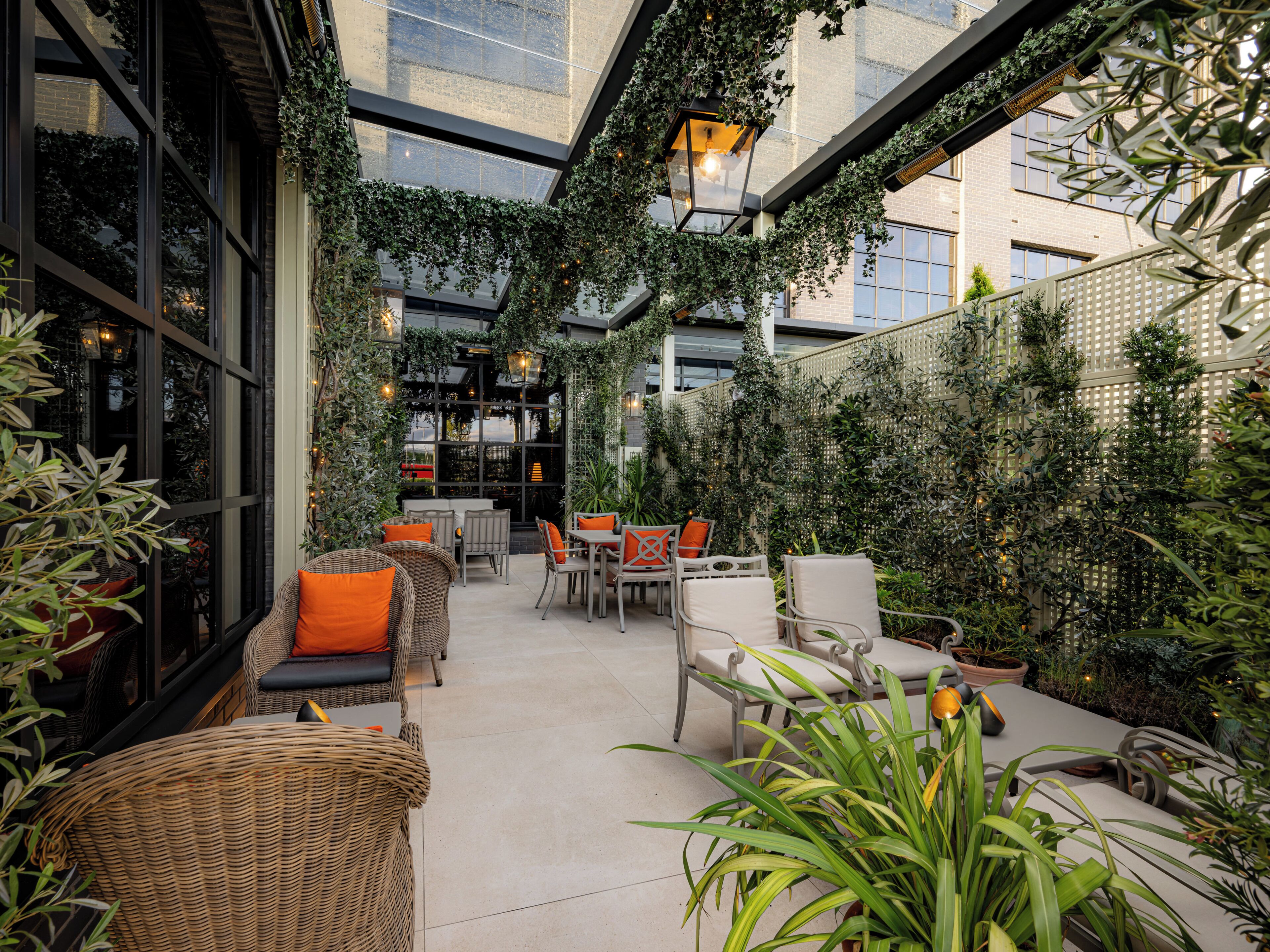 An indoor patio area with wicker furniture, potted plants, and a view of the cityscape through large windows.