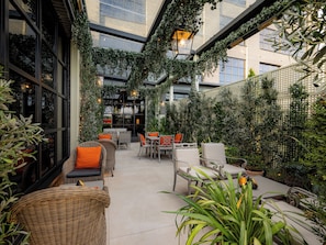 Area patio interna con mobili in vimini, piante in vaso e vista sulla città attraverso ampie finestre.